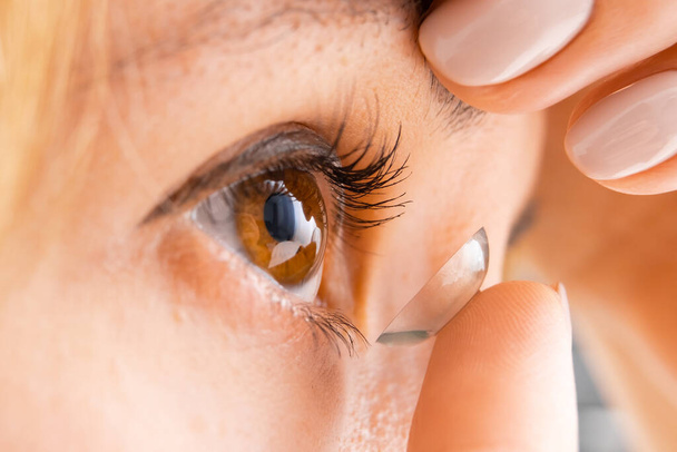 Acercamiento de la mujer joven que usa una lente de contacto para mejorar la visión. Concepto de cuidado ocular - Foto, Imagen