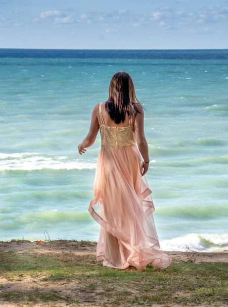 Młoda kobieta w płynącej formalnej sukni, stoi na grzbiecie wysoko nad aktywnym jeziorem, wyglądając jakby mogła skoczyć - Zdjęcie, obraz
