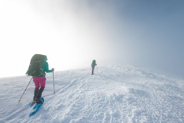 two girls walk along a mountain path in snowshoes. walking in the snow. hiking in the mountains in winter. - Zdjęcie, obraz
