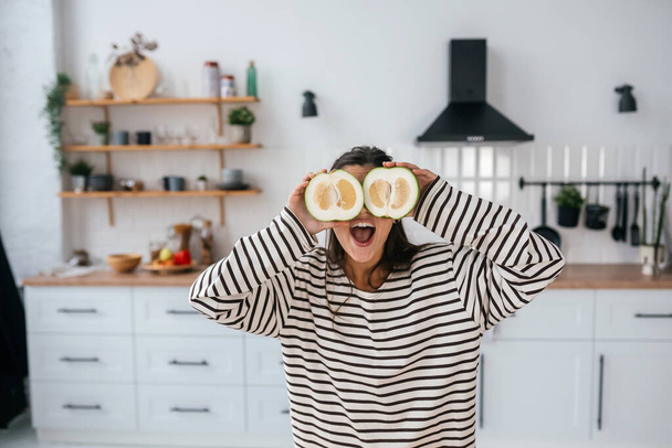 Nő tartsa vágott gyümölcs szemmagasságban helyett szemüveg a konyhában - Fotó, kép