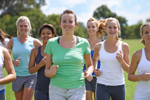 Hölkkäävät kohti parempaa terveyttä. Ryhmä nuoria naisia juoksemassa urheilukentällä yhdessä. - Valokuva, kuva