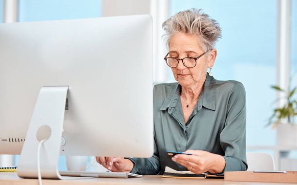 Business woman, credit card and computer with banking, online shopping and payment for bills on internet in a office. Senior woman, ecommerce and transfer money on pc at desk at her job and web app. - Φωτογραφία, εικόνα