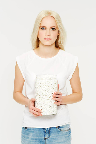 The amount of pills you take in a year. A beautiful young woman holding a jar of pills against a white background - Photo, Image