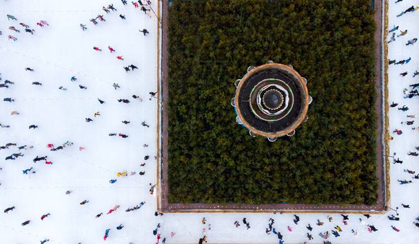 Полет беспилотника над многими людьми в разноцветной одежде на катке под открытым небом зимой. Вид сверху на городской лед. Городской парк, Ледяной каток. Зима на улице. Катание на коньках - Фото, изображение