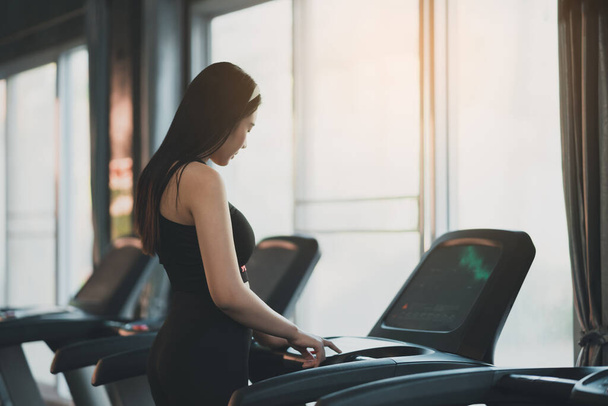 Πίσω όψη του αθλητή αθλητική γυναίκα δρομέας αγγίξει το κουμπί έναρξης πριν από την προπόνηση τρέχει στο διάδρομο στο γυμναστήριο. Καρδιο προπόνηση. Υγιεινός τρόπος ζωής, εκπαίδευση γυναικών στο γυμναστήριο. Έννοια αθλητικής λειτουργίας. - Φωτογραφία, εικόνα
