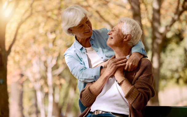 Liebe, Natur und Attrappe mit einem Senioren-Paar auf einer Parkbank, um im Ruhestand gemeinsam zu entspannen. Lächeln, Romantik und Sommer mit einem reifen Mann und einer reifen Frau, die sich im Frühling im Freien umarmen oder kleben. - Foto, Bild