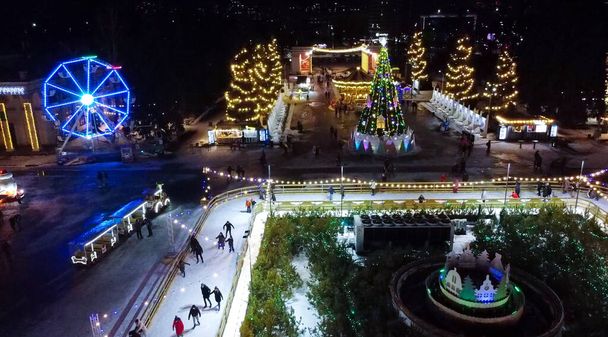Many people skating on ice skating rink in open air decorated New Year Christmas illuminations, decorations, luminous garlands on winter night. New Year Christmas holiday celebration. Aerial view - Photo, Image