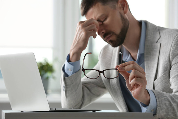 Man suffering from eyestrain in office, focus on hand with glasses - Фото, зображення