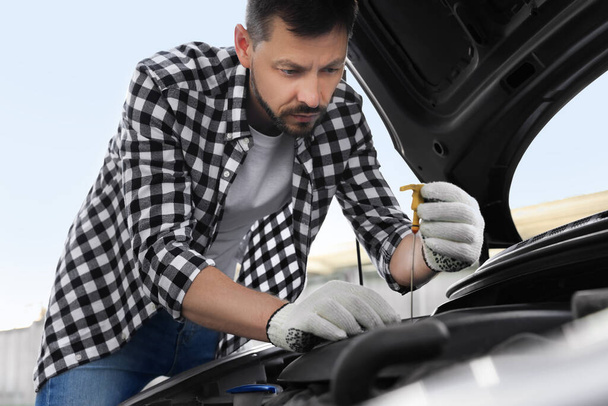 Man checking motor oil level with dipstick in car outdoors - Foto, imagen