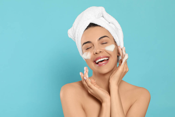 Happy jeune femme lavage visage avec des produits cosmétiques sur fond bleu clair, espace pour le texte - Photo, image