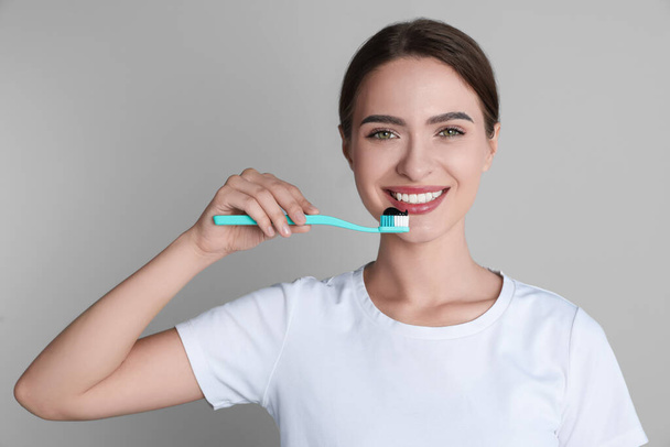 Jeune femme tenant une brosse à dents avec du dentifrice charbon sur fond gris - Photo, image