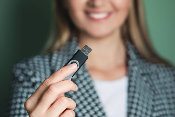 Woman holding usb flash drive against green background, focus on hand - Фото, изображение
