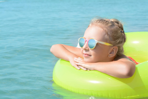 Little girl with inflatable ring in sea on sunny day, space for text - Φωτογραφία, εικόνα