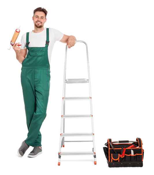 Trabalhador com adesivo de montagem perto de escada de metal no fundo branco - Foto, Imagem