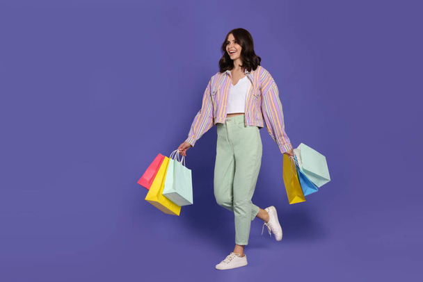 Beautiful young woman with paper shopping bags on purple background - Фото, зображення