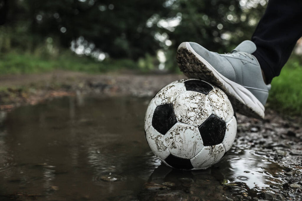 Man with dirty soccer ball in puddle outdoors, closeup. Space for text - 写真・画像