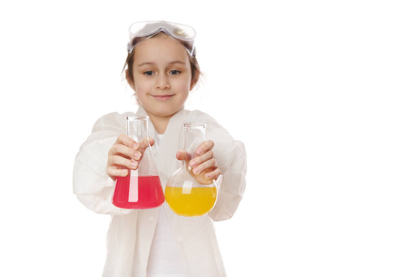Selective focus on lab flasks with chemical liquid substances, in hands of a blurred little girl, showing the current chemical reaction at chemistry lesson. Science. Early developments for smart kids - Foto, Bild
