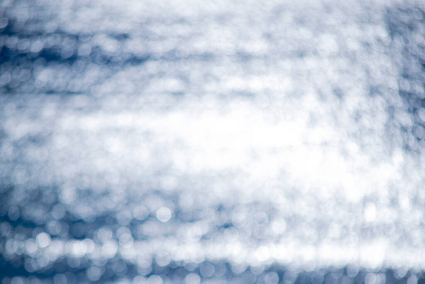 Abstraktes verschwommenes Hintergrund.Flecken von weißen Reflexen der strahlenden Sonne auf der blauen Oberfläche der Meereswellen.Meer am sonnigen Tag.Natürliche verschwommene Bokeh Textur backdrop.Seamless looping.Beautiful natürlichen Hintergrund - Foto, Bild