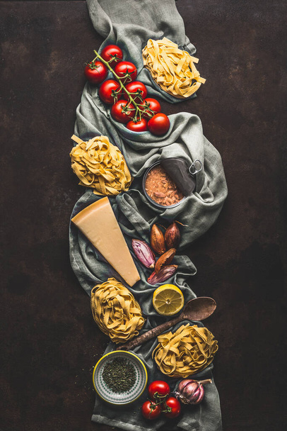 Tuna pasta cooking ingredients on dark rustic background, top view. Grocery products of Italian cuisine. Italian food. Caned tuna. Vertical. Flat lay - 写真・画像