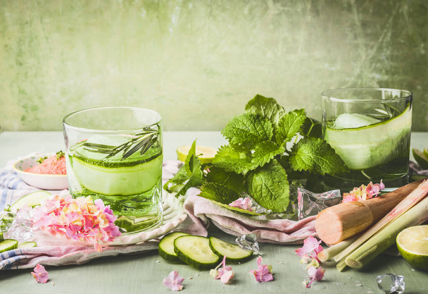 Classes with cucumber lemonade or detox infused water and ice cubes on table with ingredients. Green color summer refreshing drinks preparation - Foto, immagini