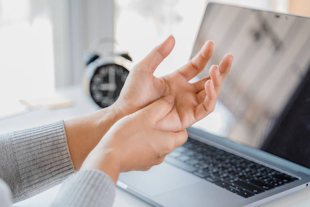 Lähikuva nainen pitelee kättään kipua käyttämästä kannettavaa tietokonetta pitkään. Toimisto oireyhtymä käsite. - Valokuva, kuva