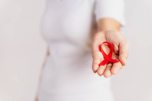 Closeup woman hand holding red ribbon HIV, world AIDS day awareness ribbon. Healthcare and medicine concept. - Zdjęcie, obraz