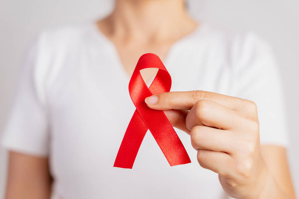 Gros plan main de femme tenant un ruban rouge VIH, ruban de sensibilisation à la Journée mondiale du sida. Concept de santé et de médecine
. - Photo, image