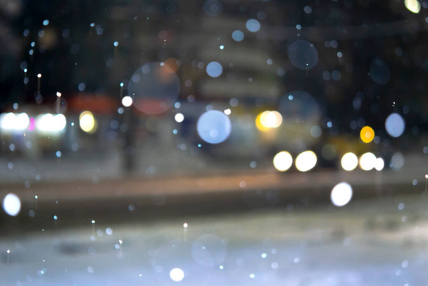 Arka plan bulanık. Şehir manzarası, ışıklar, yağan kar, gece, sokak, hareket halindeki arabaların farları. Şehirde kış manzarası olan şehir merkezini dağıtırız. Fener ışığı, kar yağışı - Fotoğraf, Görsel