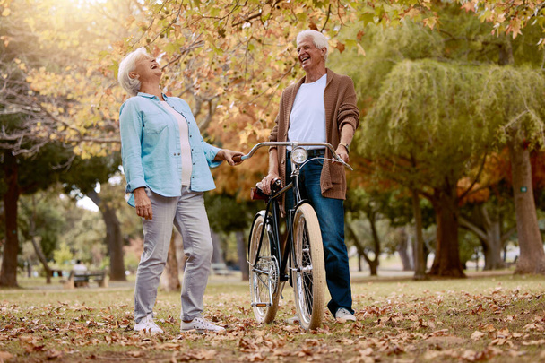 Nature, laugh and senior couple with bicycle to travel in autumn park for funny romantic date, outdoor peace or freedom. Love, retirement marriage bond and laughing man and woman with cycling bike. - Photo, Image