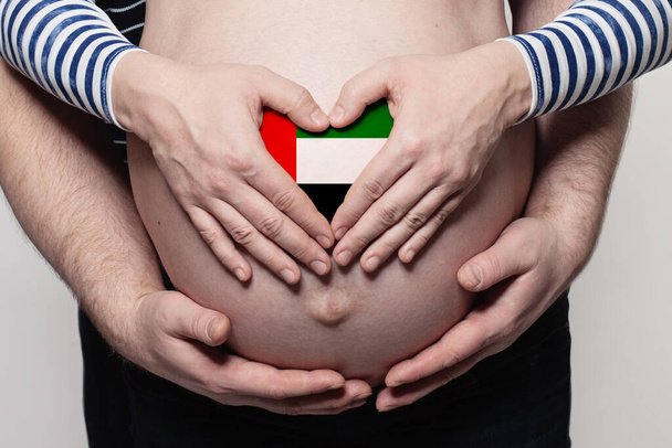 Семья в концепции OAE. Мужчина обнимает беременную женщину животом и сердцем с флагом Объединенных Арабских Эмиратов цветов крупным планом - Фото, изображение