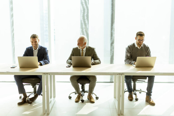 Старший бізнесмен і молоді бізнесмени працюють разом на ноутбуках в офісі
 - Фото, зображення