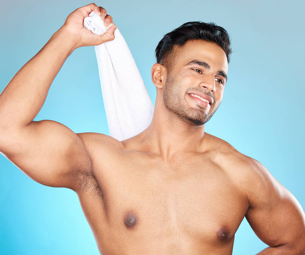 Face, skincare and body of man with towel in studio isolated on a blue background. Thinking, cleaning and personal hygiene of male model from Brazil with cotton cloth to wipe after shower or bathing - Φωτογραφία, εικόνα
