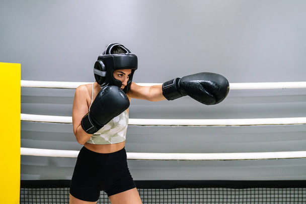 Vista lateral de una joven de pie lanzando un puñetazo hacia adelante en un ring de boxeo. - Foto, imagen