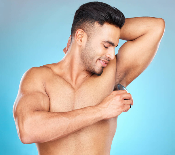 Grooming, armpit and man shaving body hair for hygiene, health and wellness on a blue studio background. Indian model for epilation with electric shaver for hair removal for clean underarm and skin. - Foto, Imagem