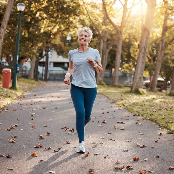 Πάρκο, τρέξιμο και καλή φυσική κατάσταση με μια ηλικιωμένη γυναίκα εξωτερική για καρδιο ή προπόνηση αντοχής το καλοκαίρι. Αθλητισμός, άσκηση και υγεία με μια ώριμη γυναίκα συνταξιούχο έξω για τρέξιμο κατά τη διάρκεια της συνταξιοδότησης. - Φωτογραφία, εικόνα