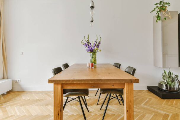 Diseño interior de estilo minimalista contemporáneo de estudio luminoso con mesa de madera y sillas en zona de comedor entre cocina abierta y sala de estar con paredes blancas y suelo de parquet - Foto, imagen