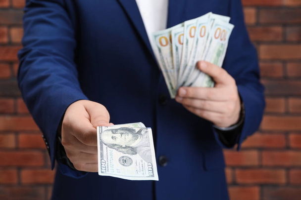 Man holding money near red brick wall, closeup. Currency exchange - Zdjęcie, obraz