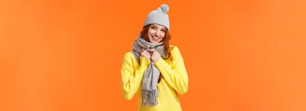 Kezd hideg lenni odakint. Aranyos és szép vörös hajú nő viselni szürke téli kalap és sál, egyre meleg felkészülés játszani hógolyókat barátaival kívül a téli ünnepek, narancs háttér. - Fotó, kép