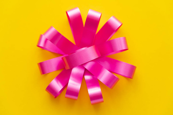 Draufsicht auf rosa Geschenkschleife auf gelbem Hintergrund  - Foto, Bild