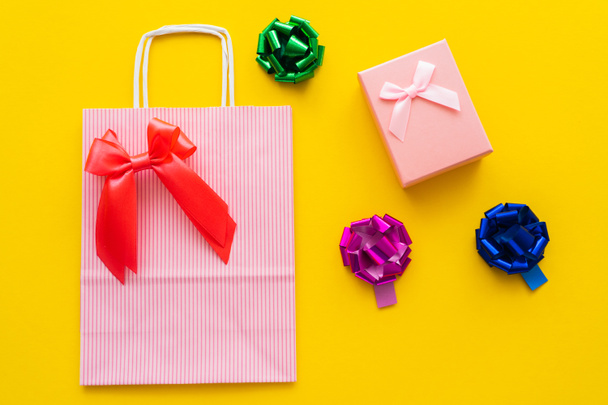 Top view of shopping bag and gift bows near present on yellow background  - Fotoğraf, Görsel