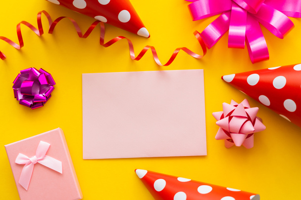 Vue du dessus de la carte de vœux près des casquettes de fête et de la boîte cadeau sur fond jaune  - Photo, image