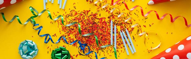 Top view of sprinkles near candles and party caps on yellow background, banner  - 写真・画像