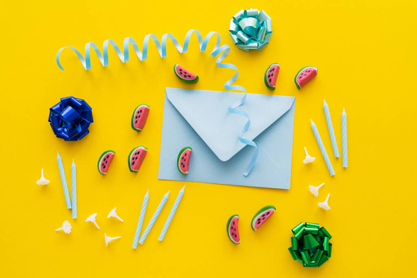 Top view of festive candles near sweets and envelope on yellow background  - Photo, Image