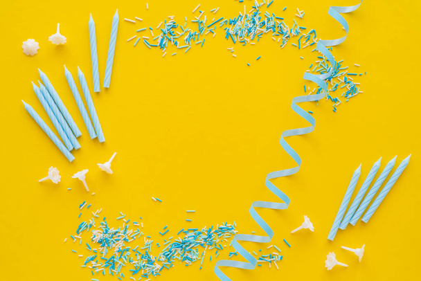 Top view of candles near blue serpentine and sprinkles on yellow background  - Photo, Image