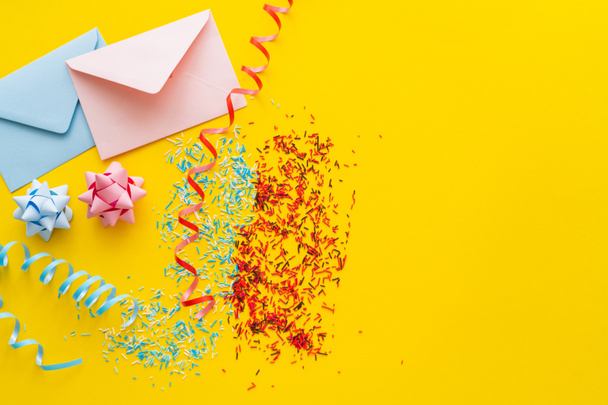 Top view of blue and pink envelopes near serpentine and sprinkles on yellow background  - Foto, Imagem