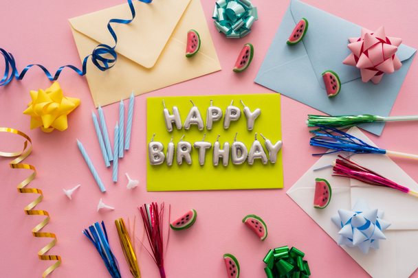 Вид сверху на свечи в форме лепестков "Счастливого дня рождения" рядом с эмалями и конфетами на розовом фоне  - Фото, изображение