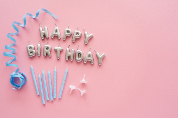 Top view of candles in shape of Happy Birthday lettering near blue serpentine on pink background  - Foto, imagen