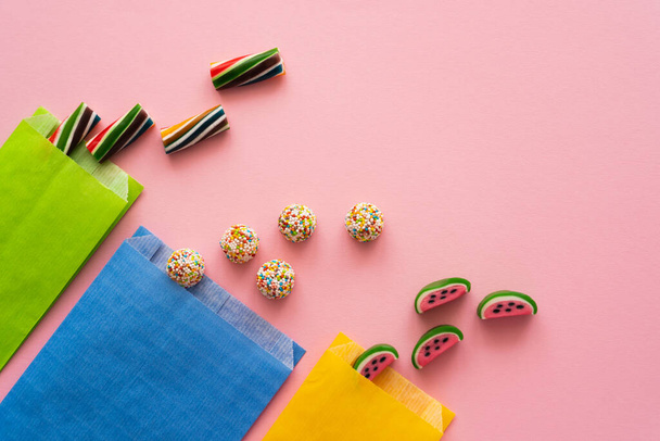 Vue du dessus des bonbons sucrés et des sacs en papier sur fond rose  - Photo, image