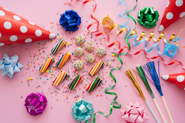 Top view of colorful sweets near serpentine and party caps on pink background  - Photo, Image