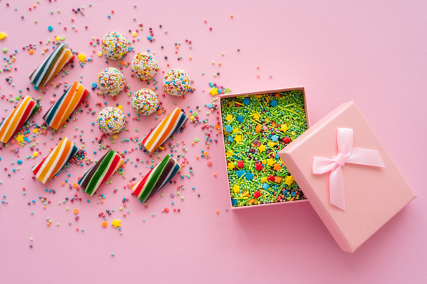 Top view of colorful sweets near gift box with sprinkles on pink background  - Photo, image